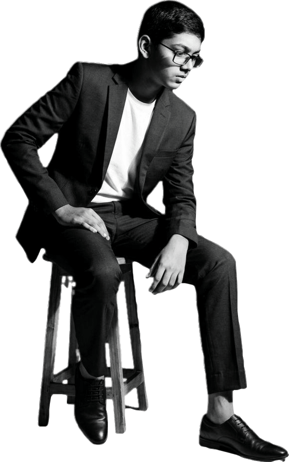 Abdullah Mohammad Zubair seated on a stool in a dark suit, full length